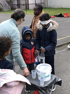 enfant les yeux bandés versant de l'eau dans un seau